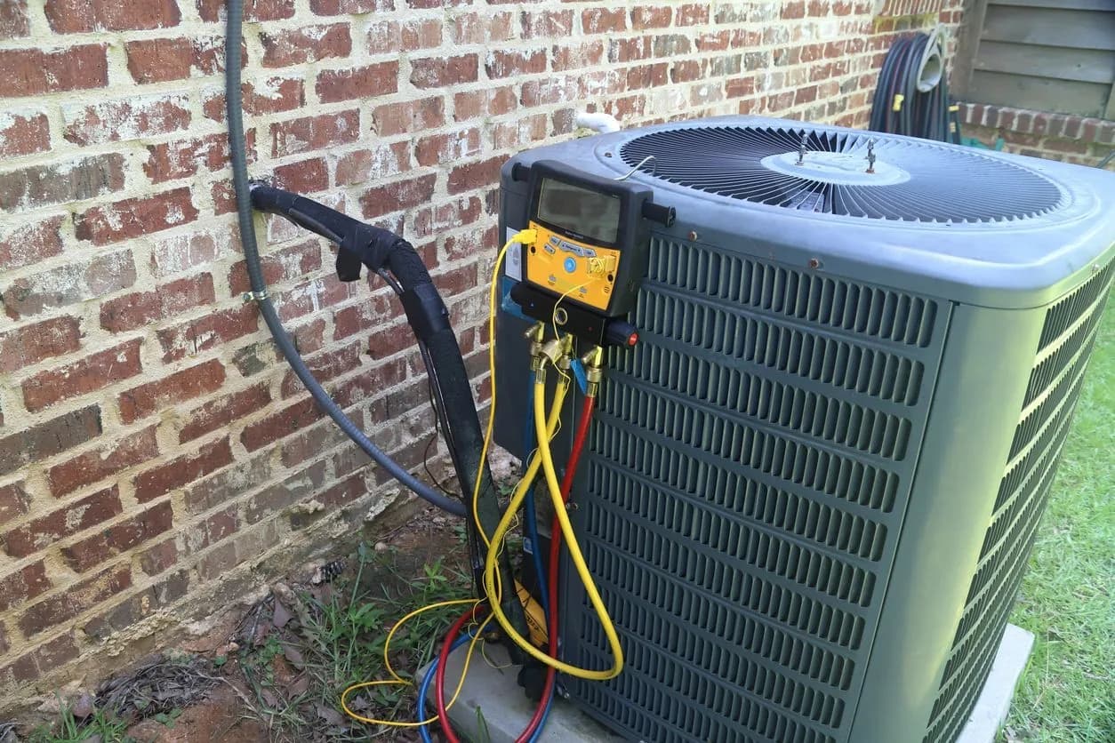 Technician's manifold gauges connected to an outdoor AC unit during an inspection